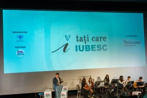 Scena evenimentului „Tați care iubesc” 2026, cu muzicieni și sigla Artesana proiectată pe ecran, alături de organizatori și parteneri.