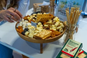 Un platou din lemn încărcat cu brânzeturi uscate/maturate Artesana, caise uscate, biscuiți și grisine.