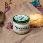 Cremă de brânză Artesana, în borcan de sticlă, servită alături de o chiflă.