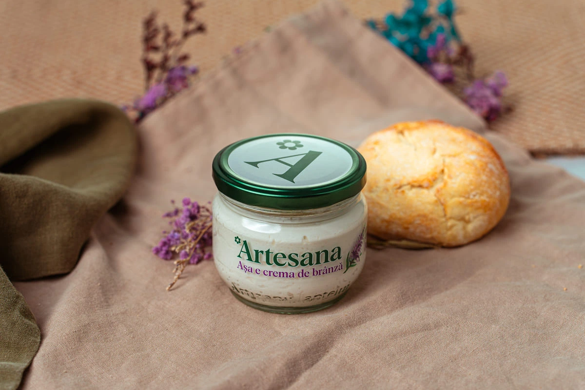 Cremă de brânză Artesana, în borcan de sticlă, servită alături de o chiflă.