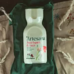 Sticlă de lapte de vacă Artesana, așezată pe un material verde și un șervet textil decorat cu broderii florale și spice uscate.